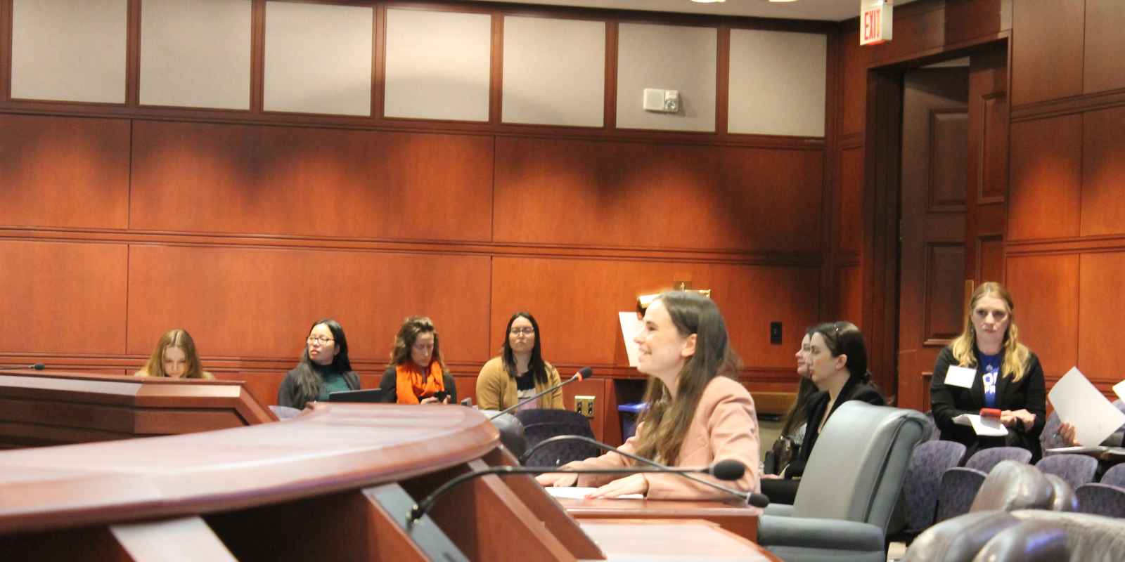 Jess, a white woman, wearing a pink blazer is testifying at the Capitol.