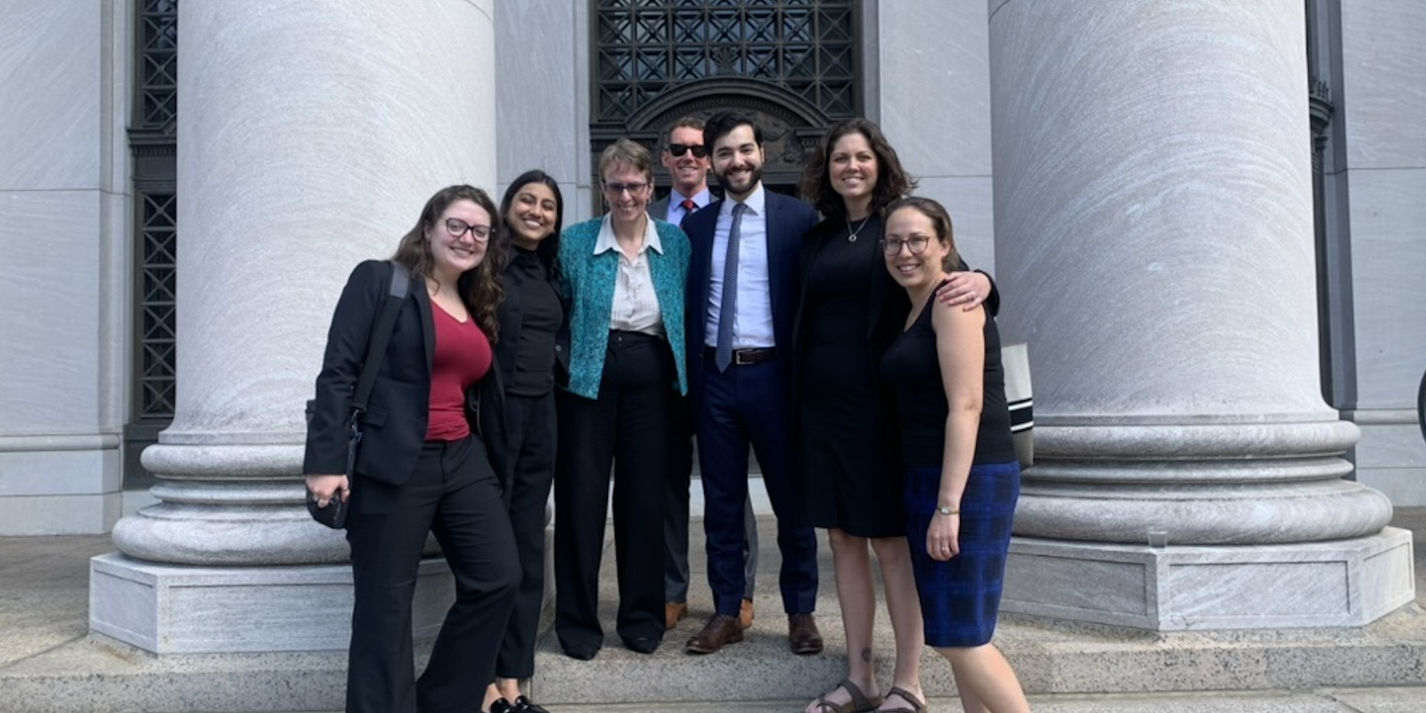 In front of the court, our legal team plus co-counsel stands on the steps and smiles at the camera.