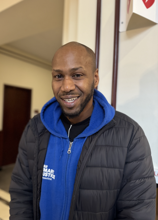 Chris, a Smart Justice Leader, is smiling at the camera wearing one of the smart justice zip ups.