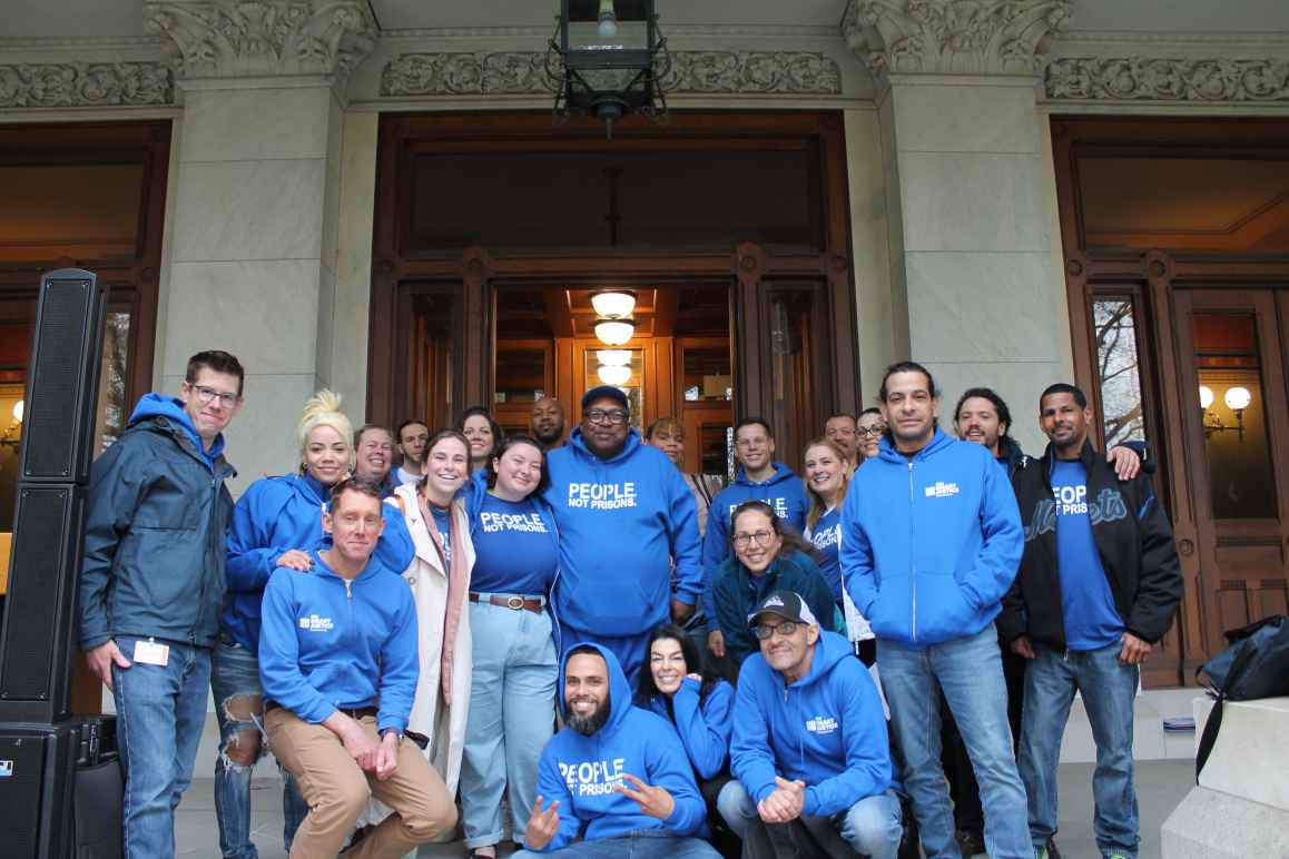A group of approximately 20 people wearing ACLU bright blue t-shirts smiling at the camera, standing in front of the Capitol building in Hartford, Connecticut.