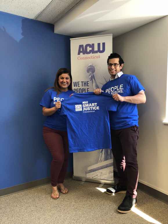 Melvin Medina and Sandy Lomonico, ACLU Smart Justice Connecticut, hold &quot;people not prisons&quot; shirts in front of ACLU-CT banner