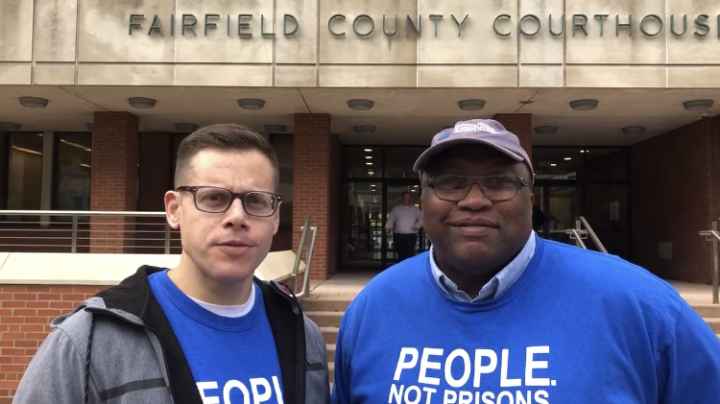 ACLU-CT Gus Marks-Hamilton and Anderson Curtis in blue "people, not prisons" shirts, stand outside of the Fairfield County Courthouse