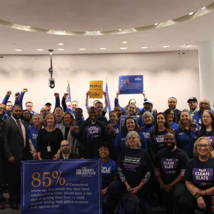 ACLU of Connecticut Smart Justice, CONECT, GHIAA, and Connecticut state legislators stand and sit in a group to support Clean Slate, behind a blue banner with a statistic about voters' support for Clean Slate ideas.