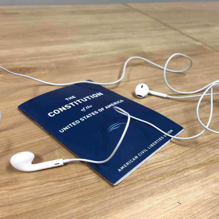 A blue Constitution of the United States, published by the ACLU, sits on a table under white headphones