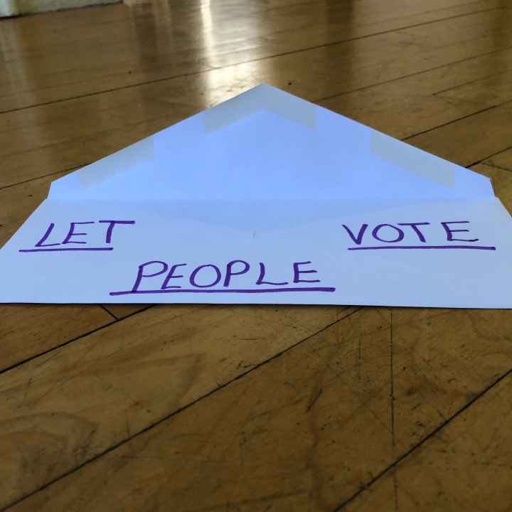 a white envelope against wood background. written on the envelope: LET PEOPLE VOTE