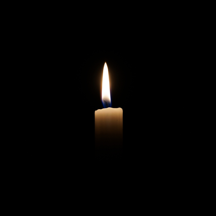 a white candle, lit, is in the center of the frame. The rest of the image is a black square