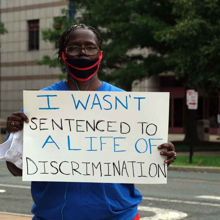 ACLU-CT Smart Justice leader stands with sign: I wasn't sentenced to a life of discrimination